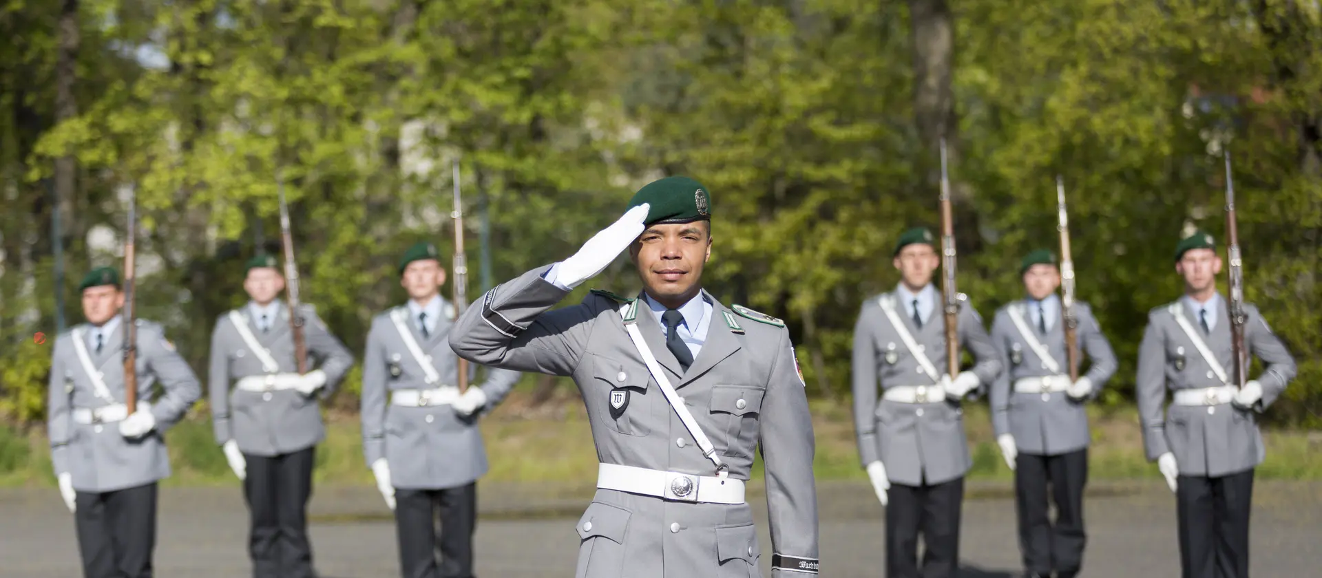 Soldaten im Protokolldienst stehen angetreten in einer Formation, grüßen und präsentieren das Gewehr.