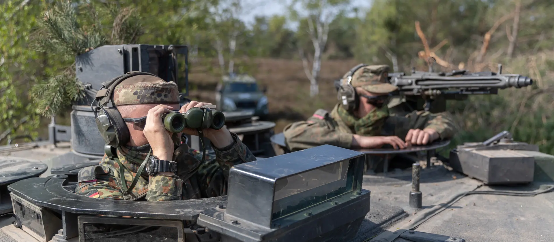 Soldaten mit Fernglas und Maschinengewehr schauen aus der Luke eines Panzers.