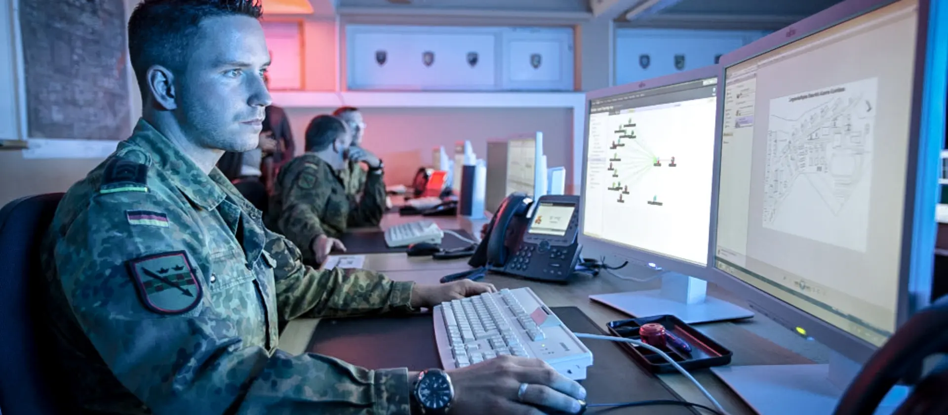 IT-Administrator in Uniform sitzt vor seinen Monitoren.