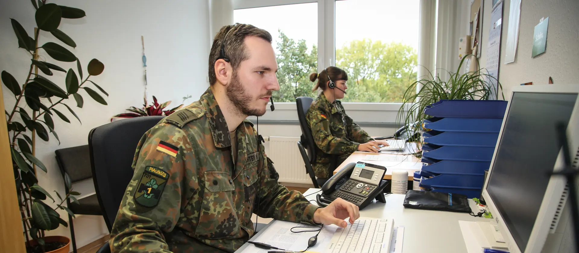 Ein Soldat sitzt mit seiner Kameradin am Schreibtisch und arbeitet am Computer.