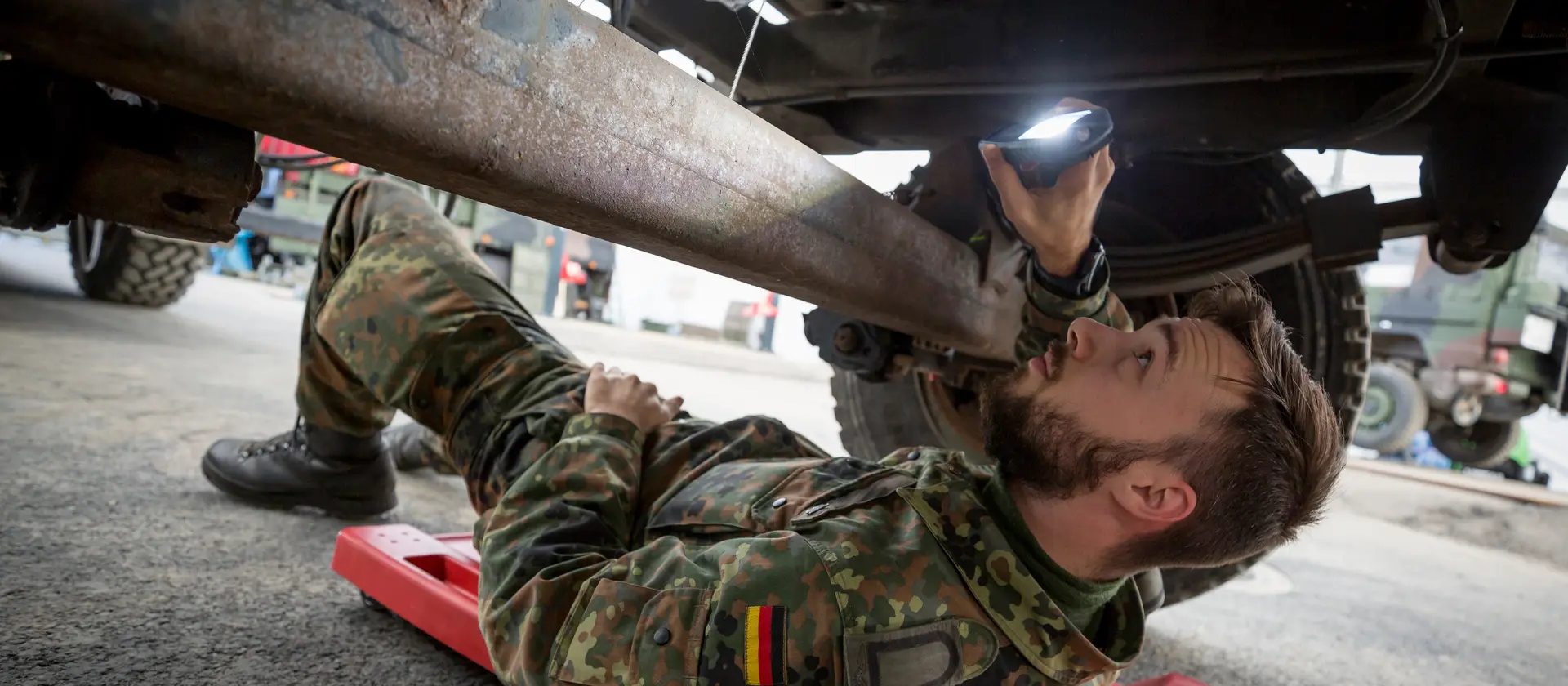 Ein Soldat liegt unter einem Fahrzeug und repariert eine Achse.