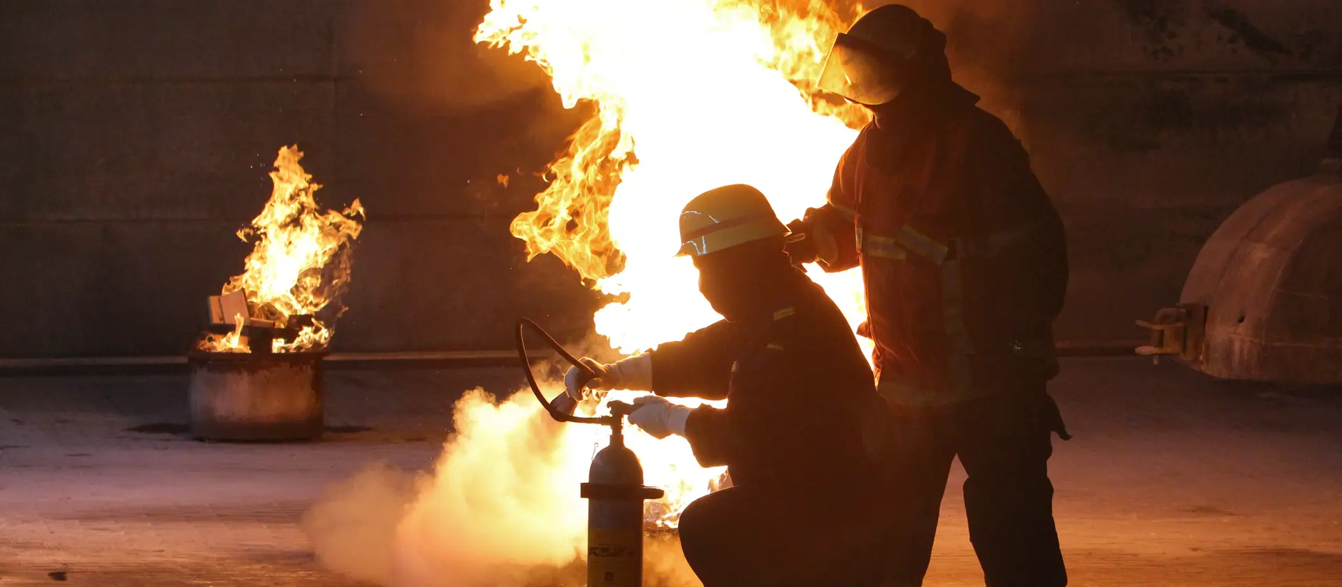 Feuerwehrleute löschen ein brennendes Fass.