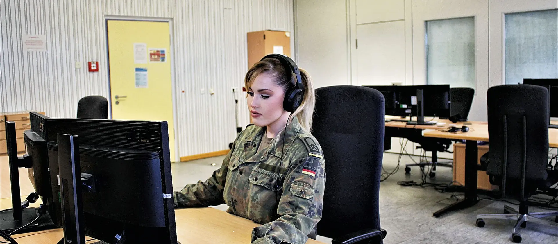Eine Soldatin sitzt mit Headset vor einem Computer