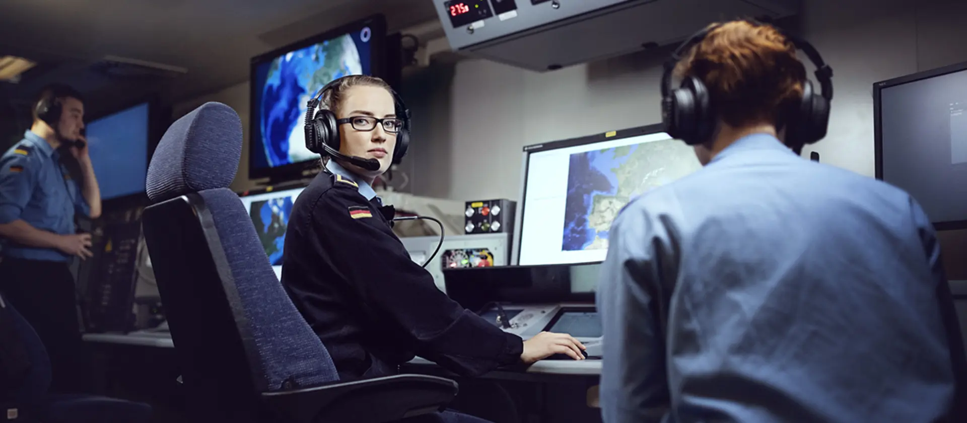 Eine Soldatin der Marine sitzt mit Kopfhörern vor Monitoren.