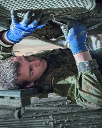 Ein Soldat liegt unter einem Fahrzeug, um es zu reparieren.