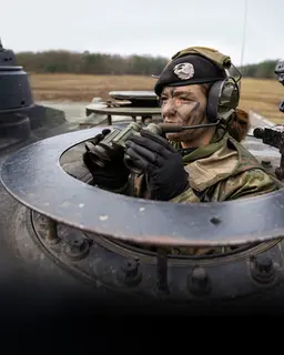 Eine Soldatin schaut mit einem Fernglas in der Hand aus einem Panzer