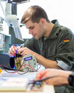 Mann misst mit einem elektronischen Messinstrument die Verkabelung eines technischen Gerätes