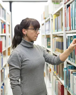 Frau schaut in einer Bibiliothek auf ein Regal mit Büchern