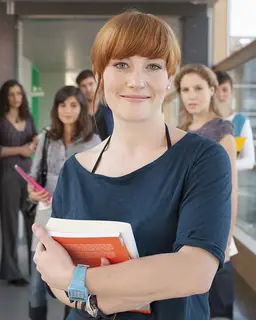 Eine Gruppe Frauen und ein Mann steht mit Büchern in einem Gang mit Glasfenstern